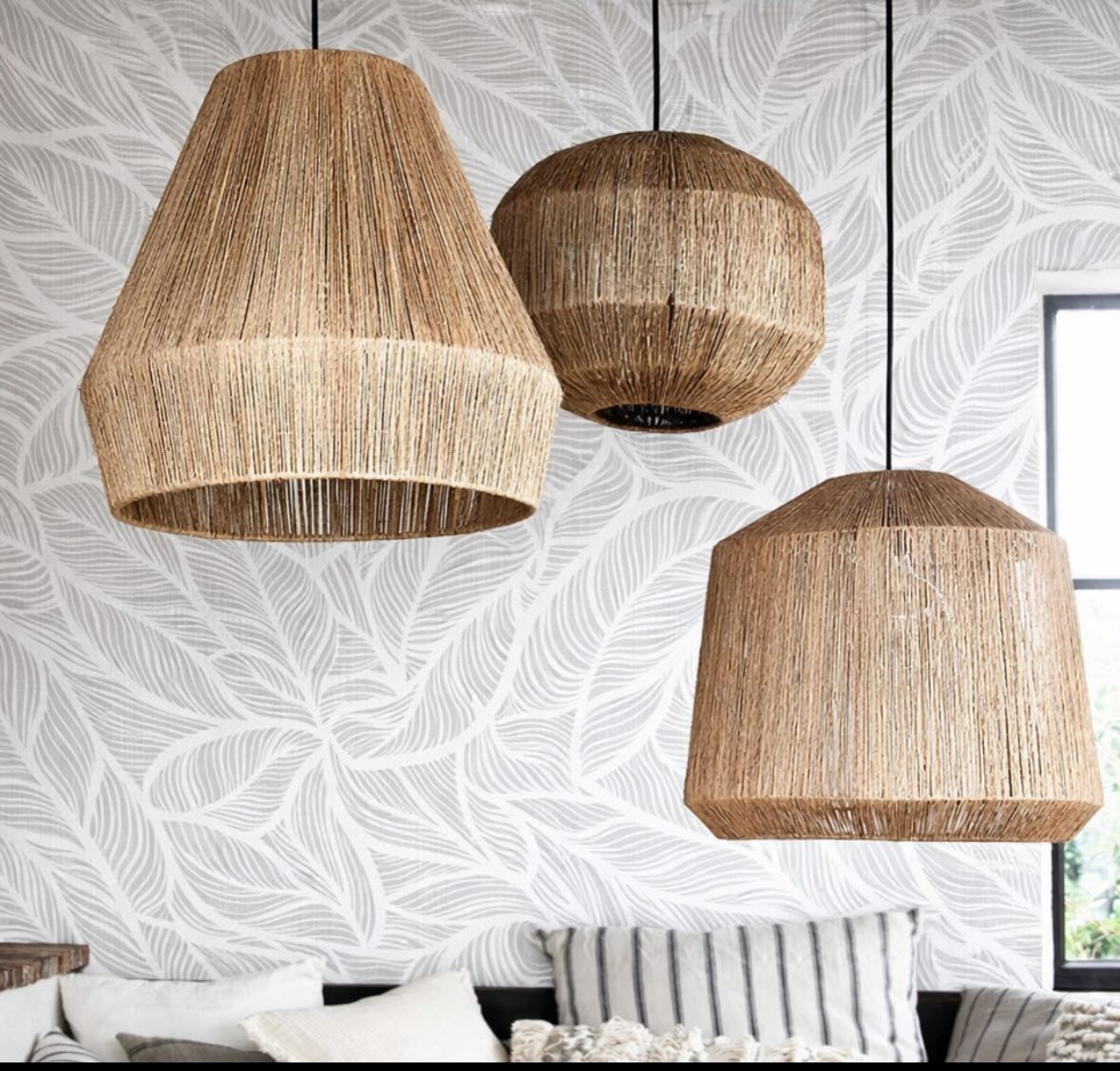 Three large woven jute pendant lights hanging against a leaf-patterned wallpaper background.