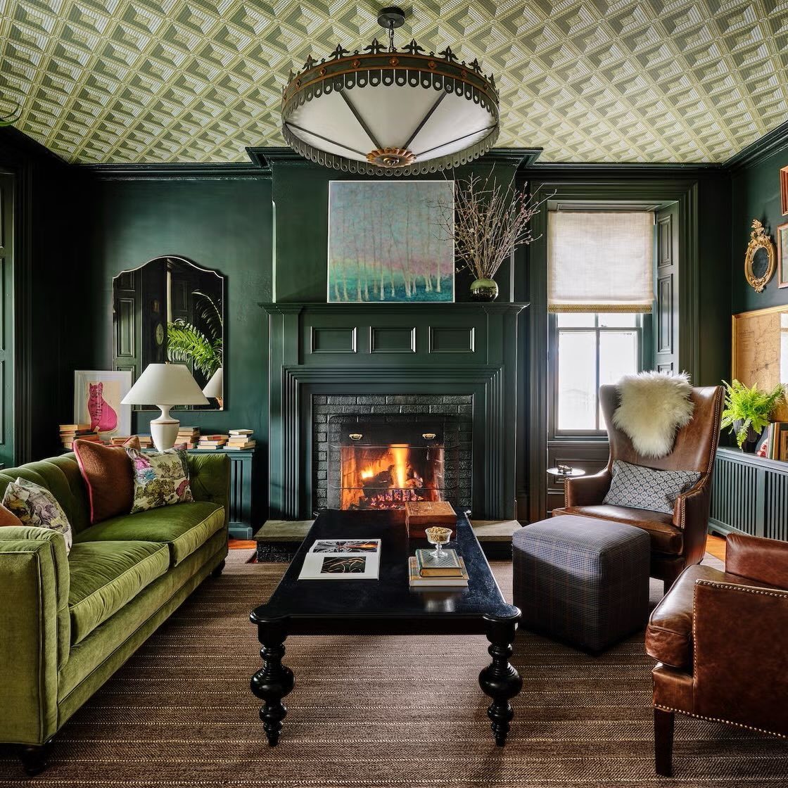 Dark green living room with a fireplace, green velvet sofa, and patterned ceiling.