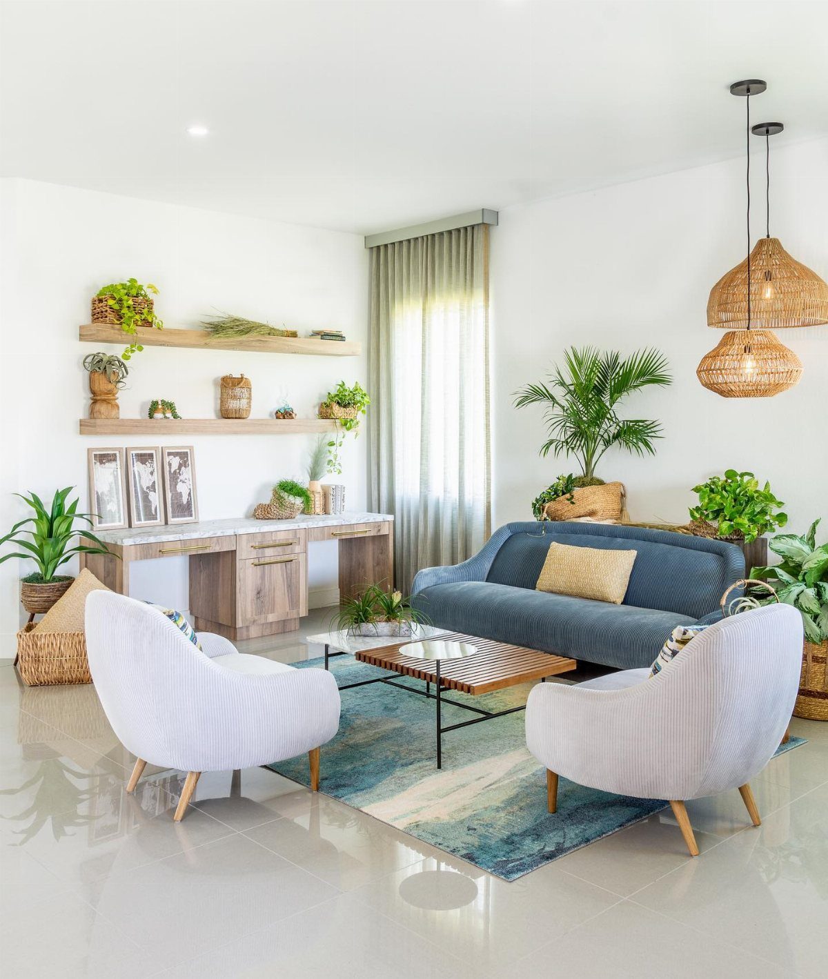 A bright boho living room with a blue sofa, white armchairs, woven lights, and many green plants.
