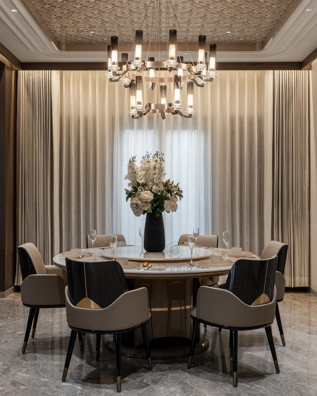 A round dining table with a large white floral centerpiece and a modern chandelier.