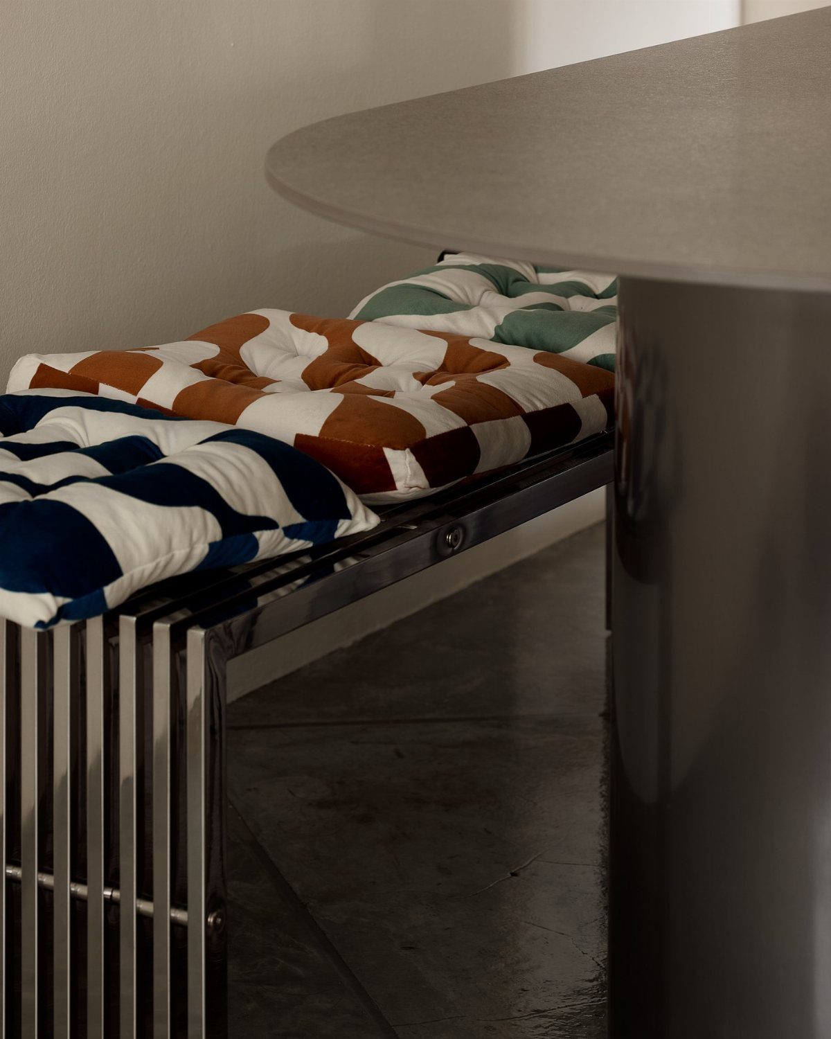 Patterned tufted cushions resting on a silver metallic slatted bench under a round table.