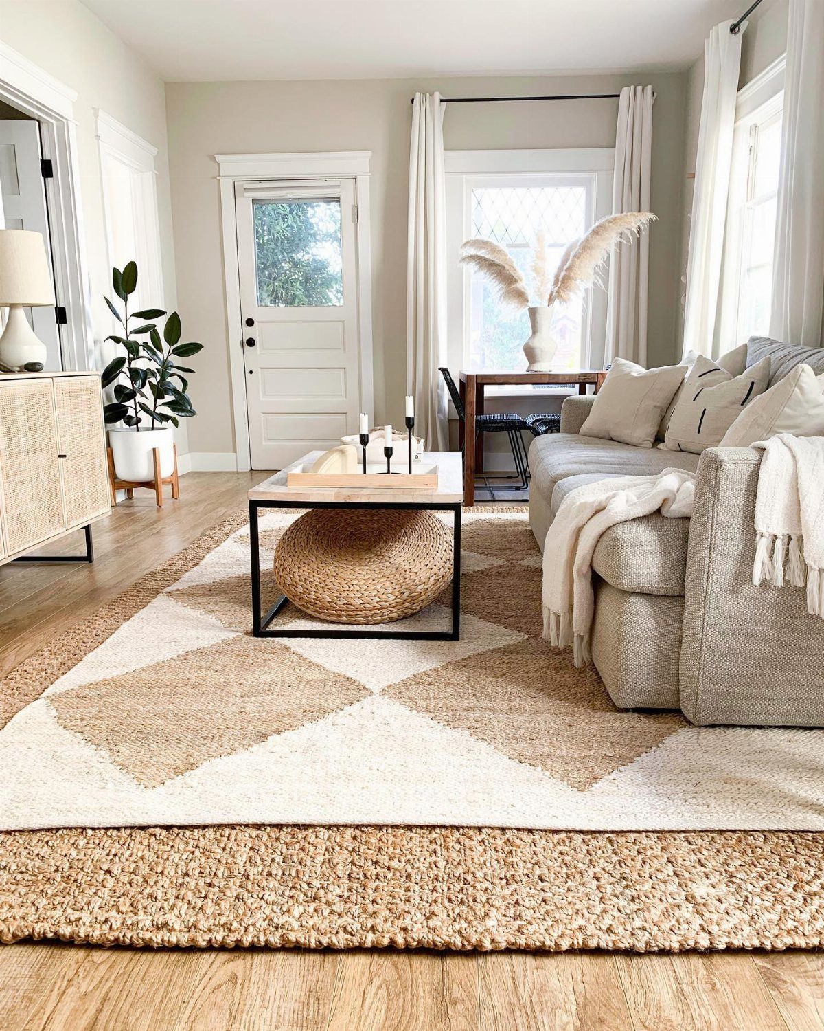 Layered geometric and textured rugs in a bright living room with a sofa and coffee table.