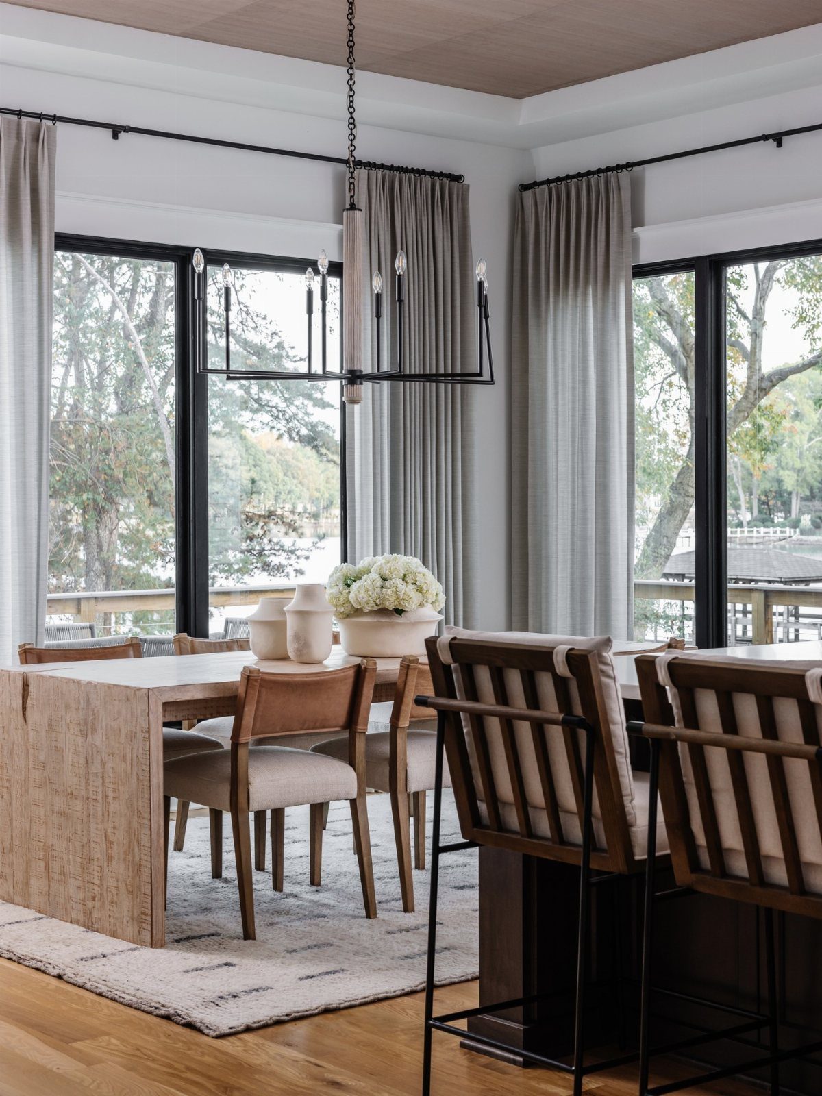A light wood dining table with tan chairs under a black linear chandelier.