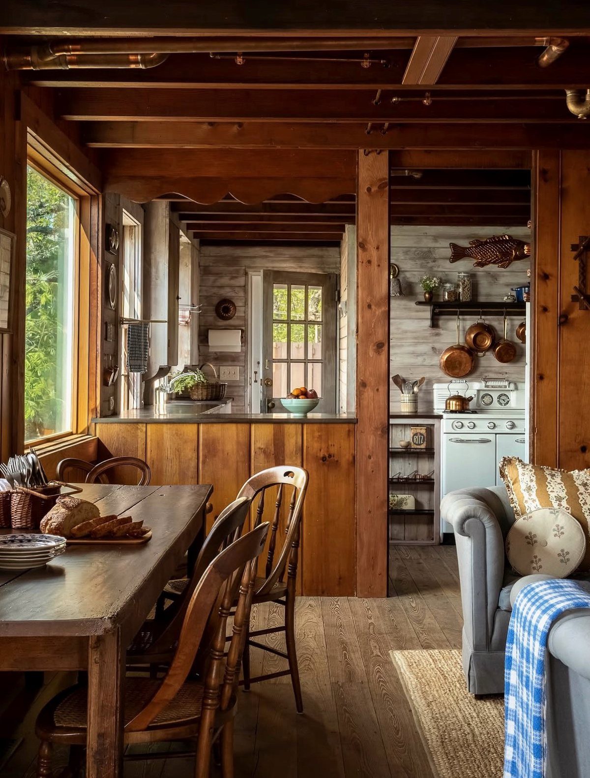 Rustic dining room with a wooden table, mismatched chairs, and warm wood paneled walls.