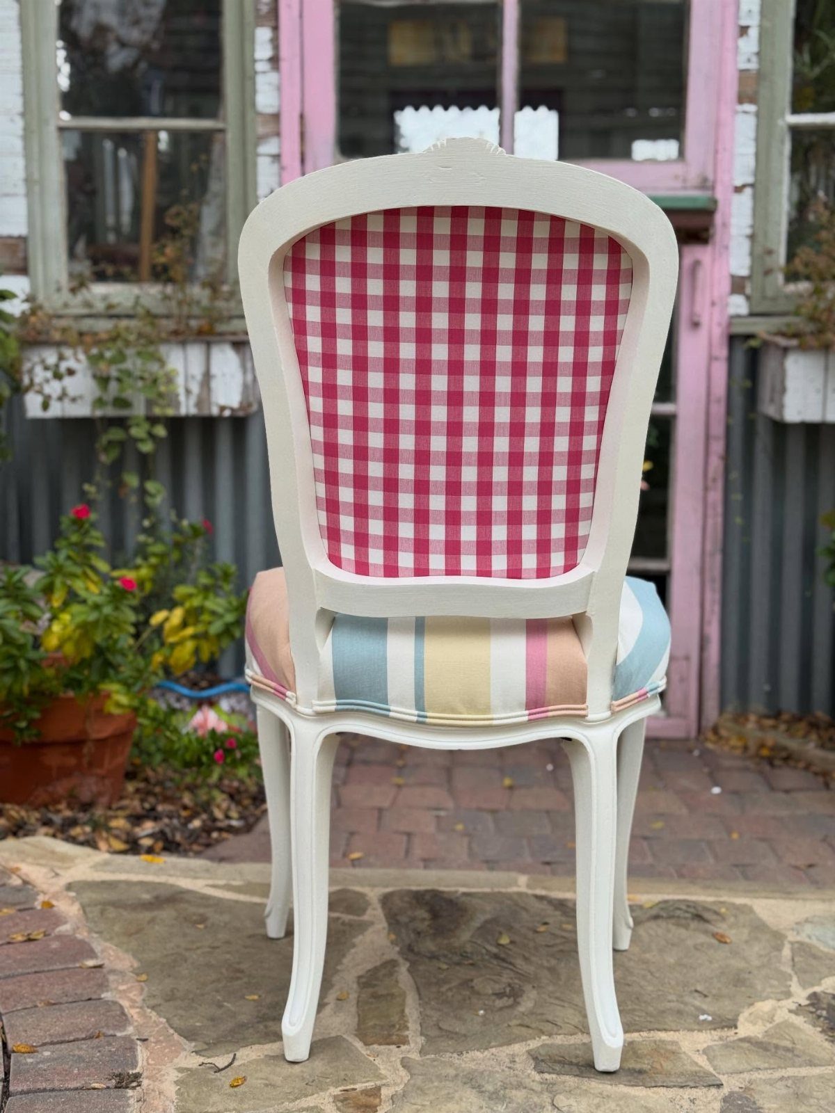 A white wooden chair featuring a pink gingham back and a multi-colored striped seat cushion.