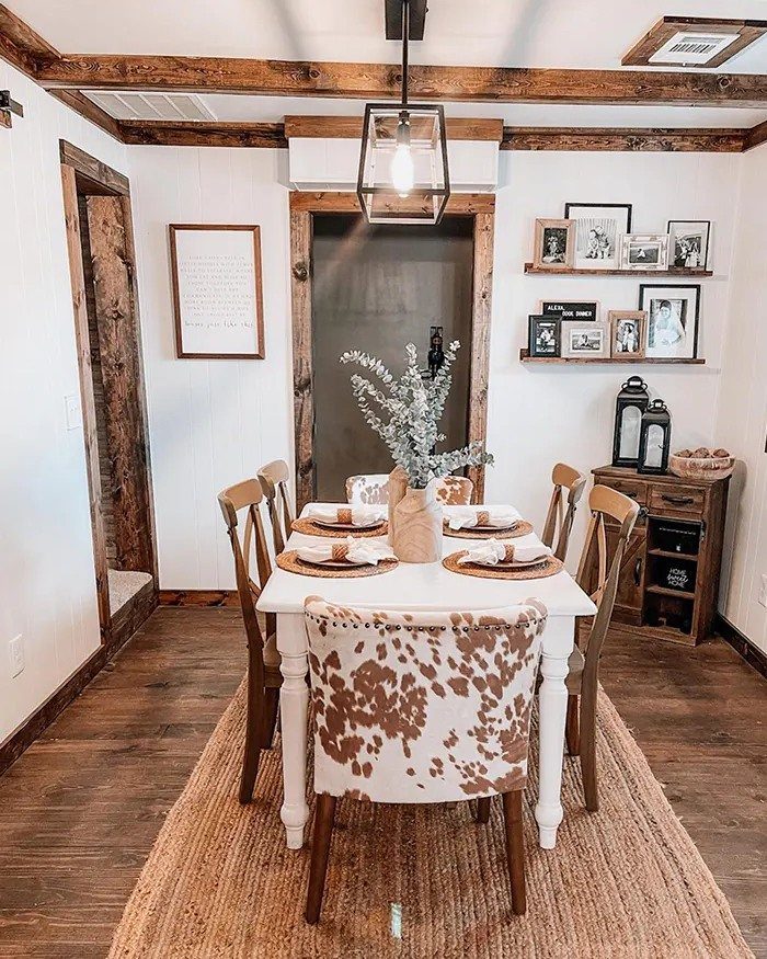A white dining table set for a meal with wooden chairs and a cowhide accent chair on a jute rug.