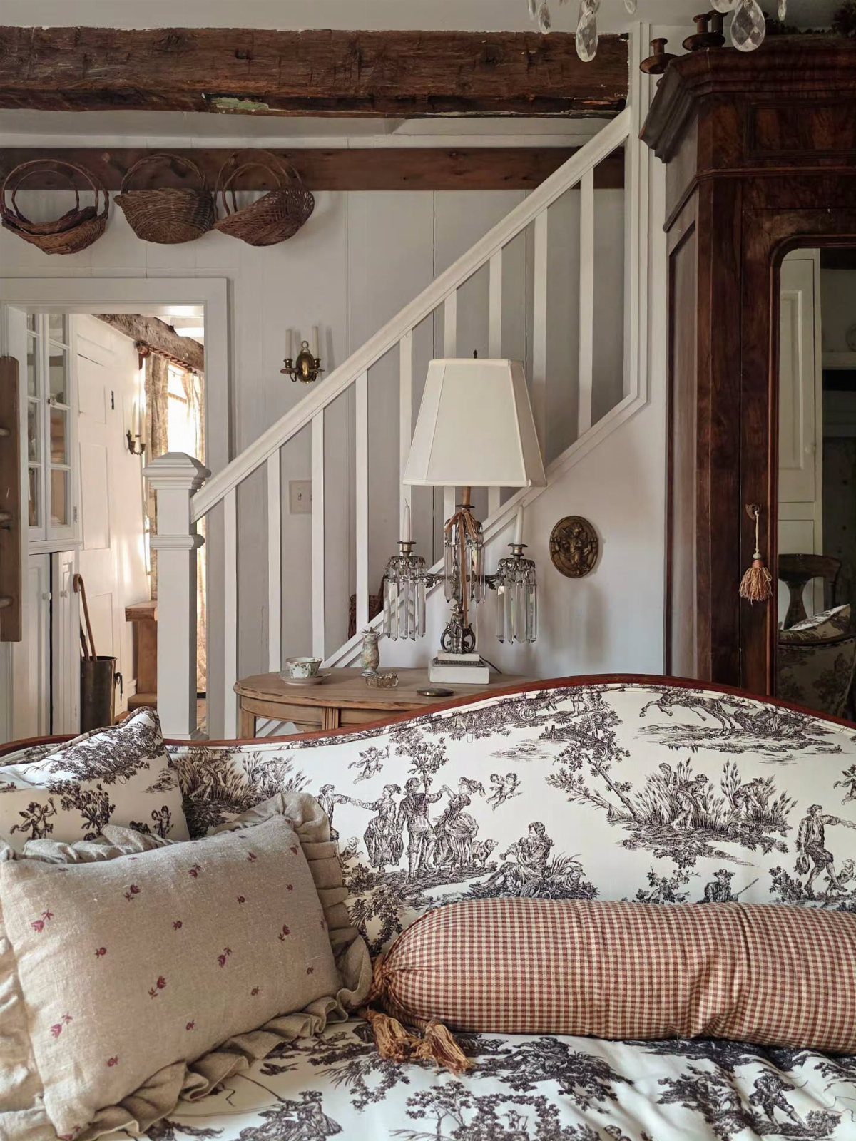 A toile patterned sofa with neutral pillows sits in a room with a white staircase.