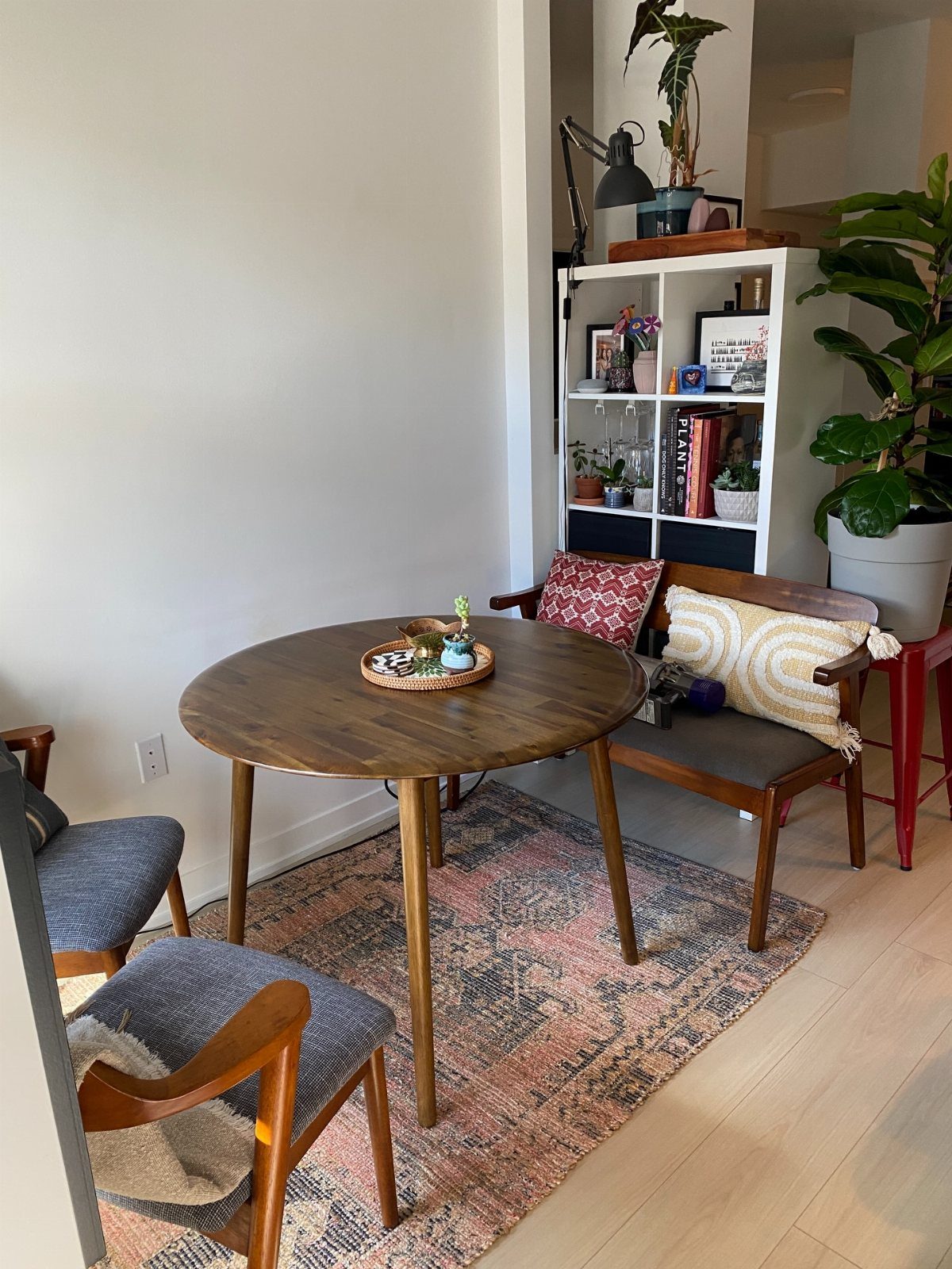 A round wooden dining table with blue chairs and a wooden bench on a patterned rug.