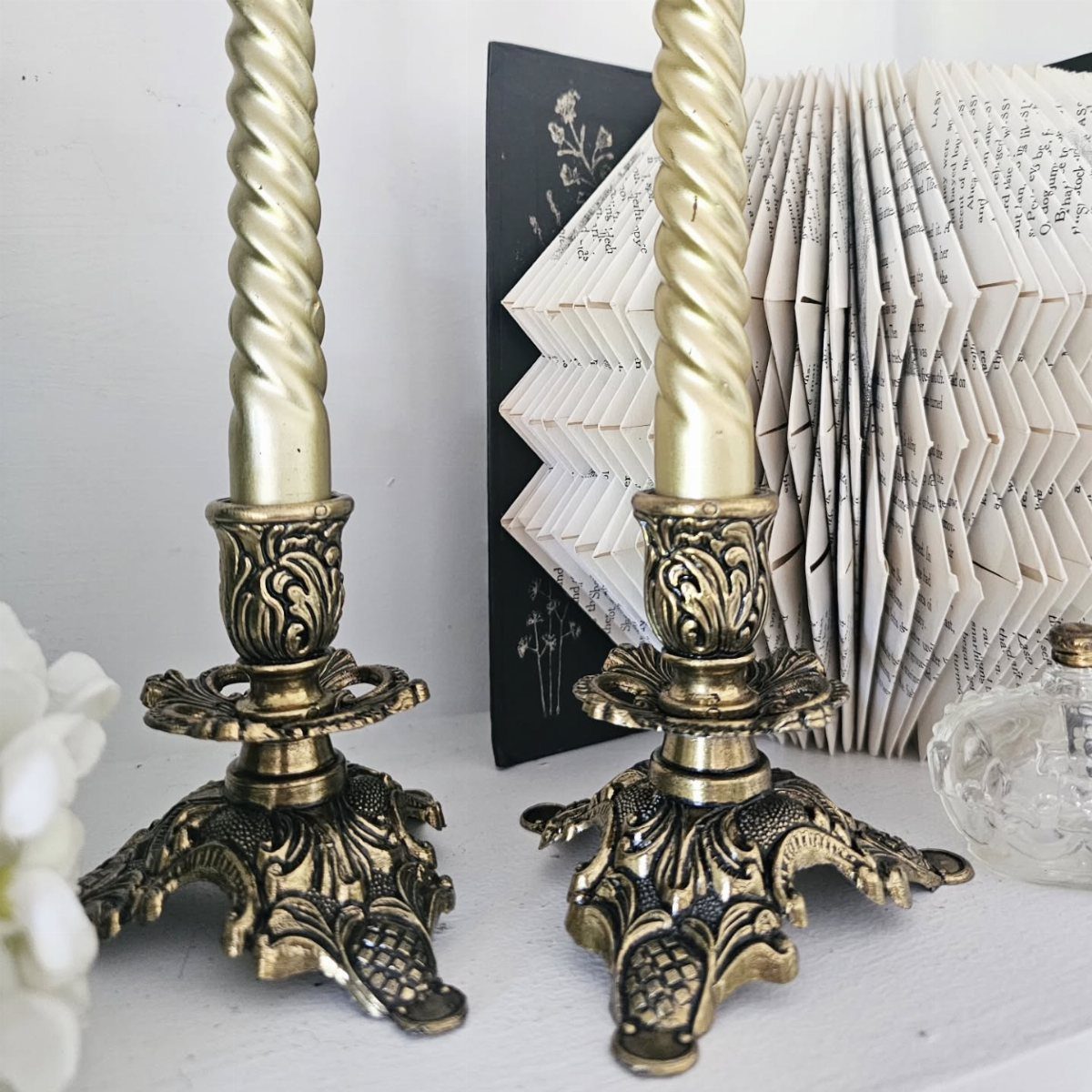 Two ornate brass candlesticks with twisted cream candles on a white surface.