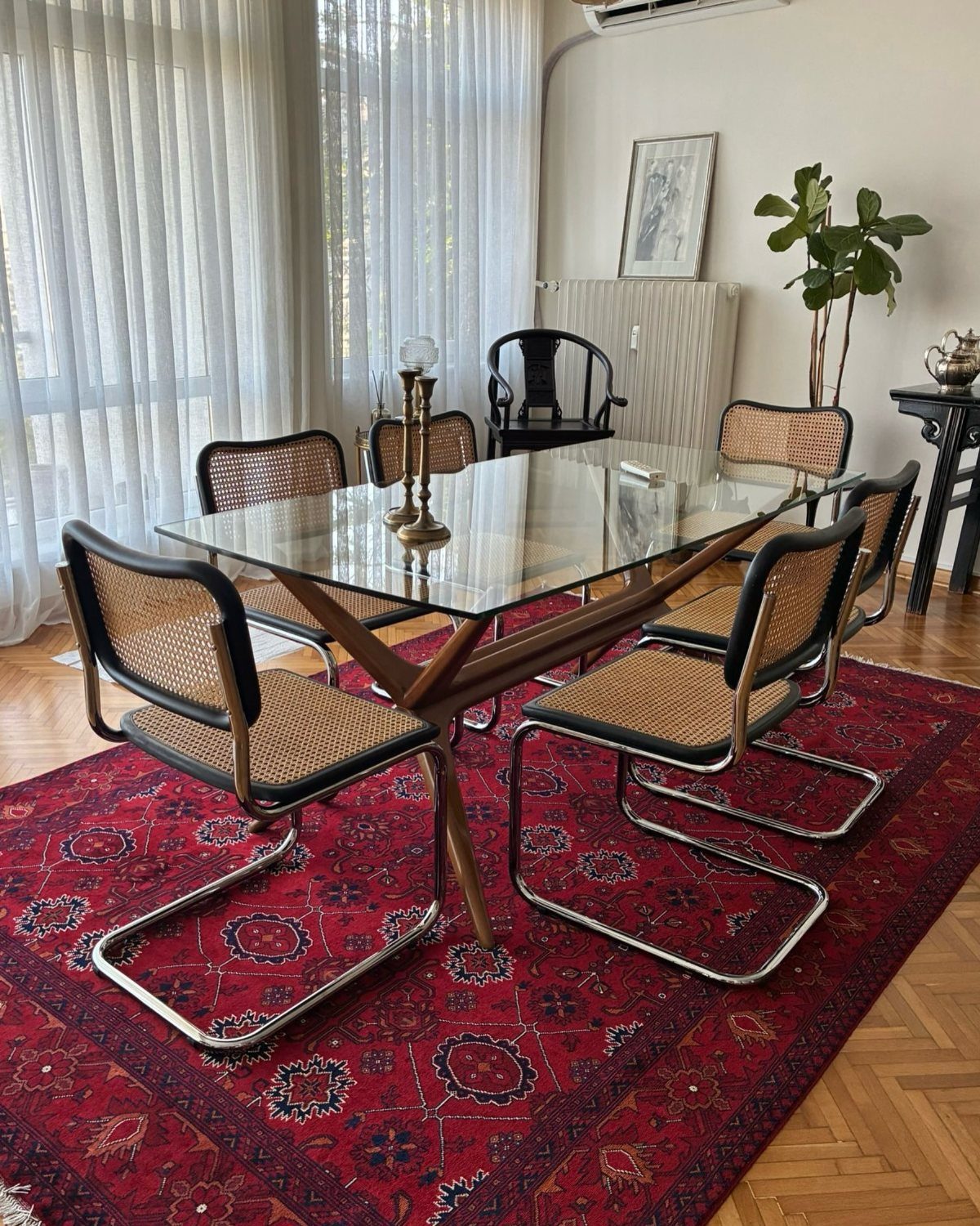 Mismatched dining chairs surrounding a glass table on a large red patterned rug.