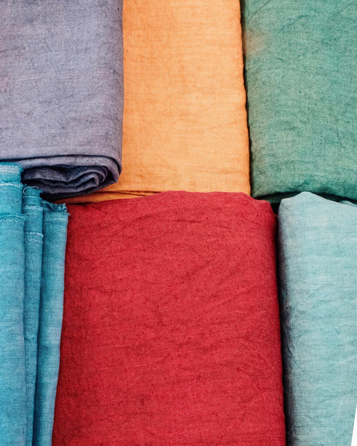 Folded colorful textured linens in red, orange, teal, and blue arranged together.