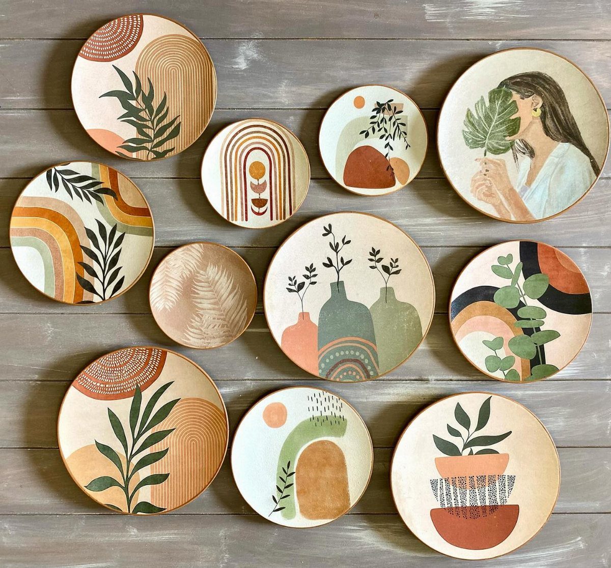 Decorative ceramic plates with botanical and abstract boho designs arranged on a grey wooden wall.