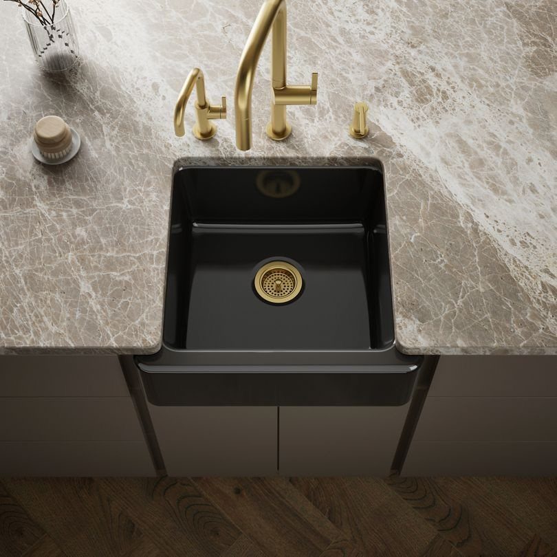 A black farmhouse sink with gold hardware installed in a marble countertop.