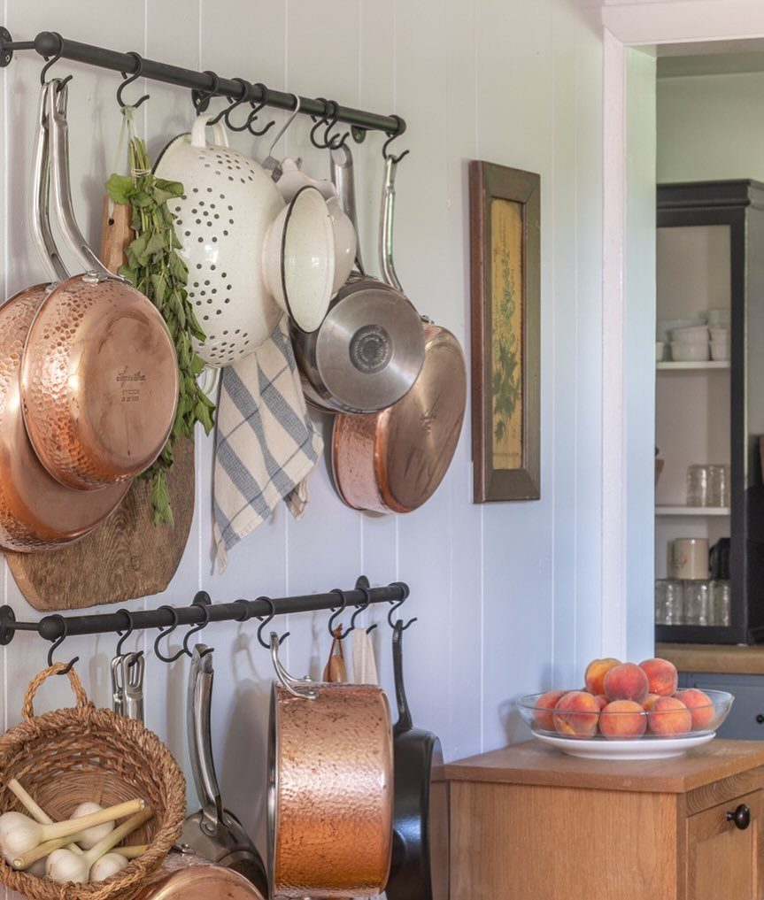 Copper cookware and a white colander hanging from black metal rails on a white wall.