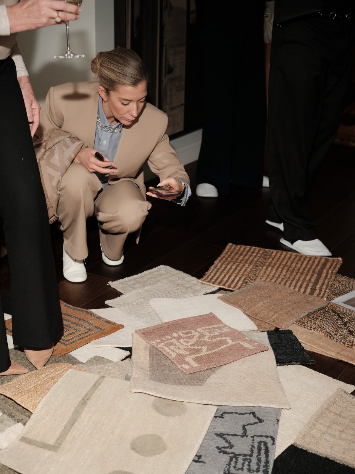 A woman kneels on a dark floor examining various small textured rug samples.