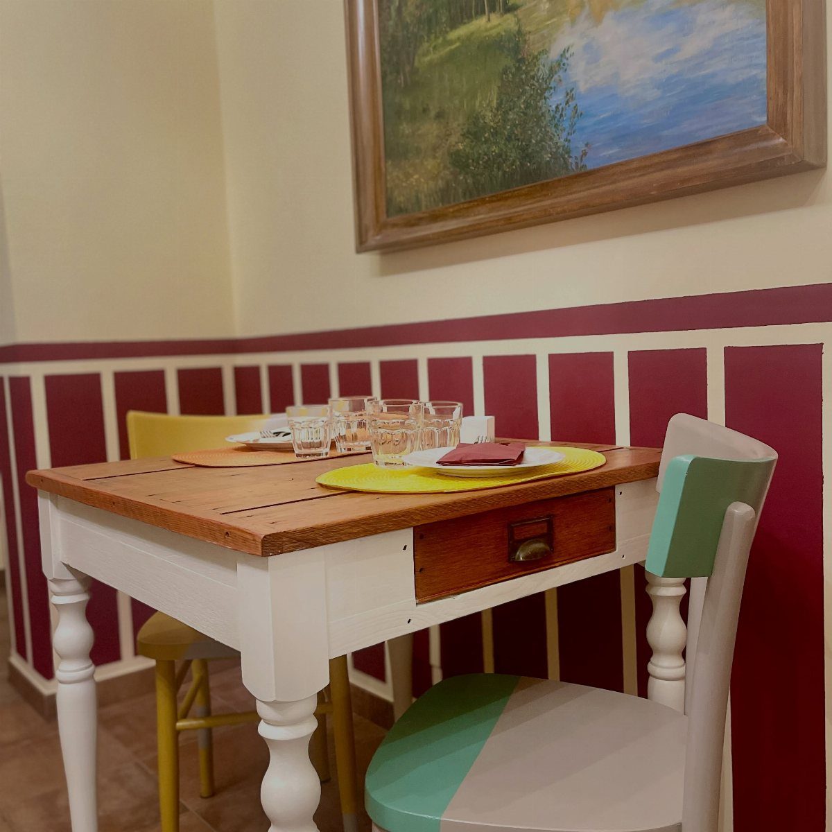 A small wooden dining table with mismatched yellow and white painted chairs against a red paneled wall.