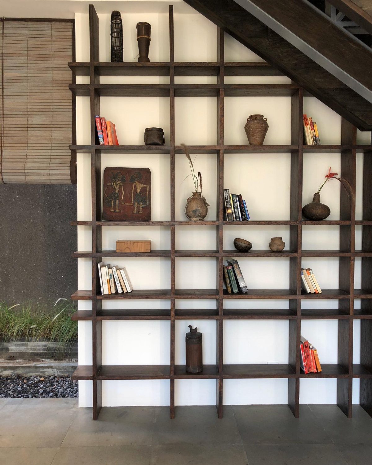 Dark wood open shelving unit displaying eclectic ceramic vases, books, and decorative pottery pieces.