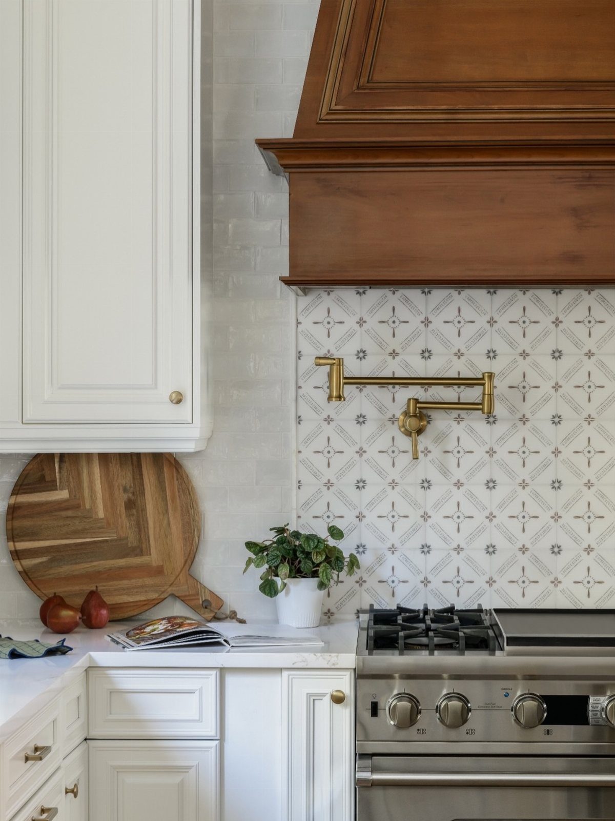 Patterned grey and white tiles serve as a backsplash behind a brass pot filler and stove.