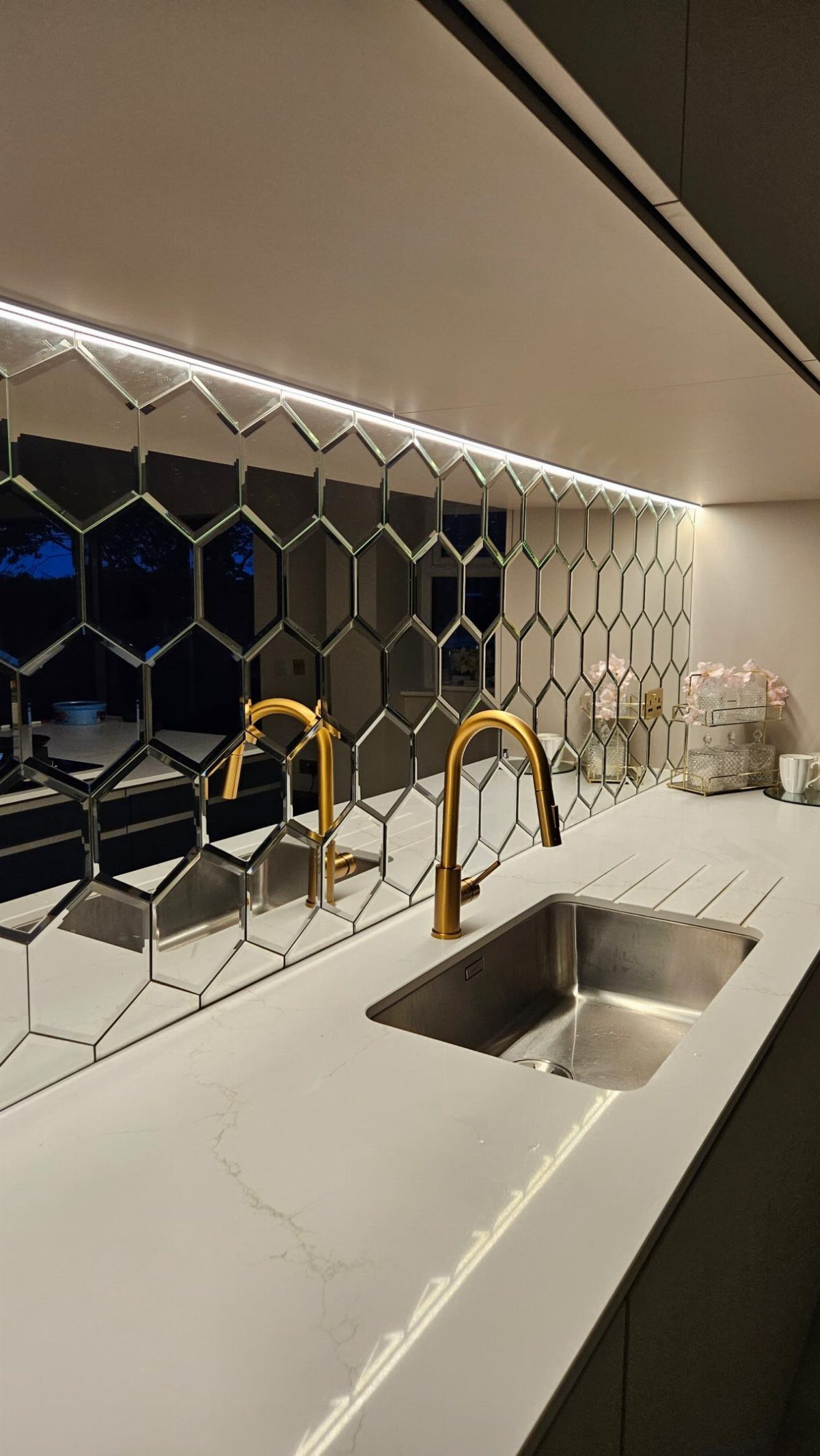 Hexagonal mirror tiles create a geometric backsplash above a white marble kitchen countertop and sink.