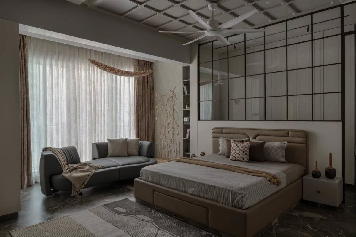 Modern bedroom with layered grey and brown bedding, a chaise lounge, and sheer white curtains.