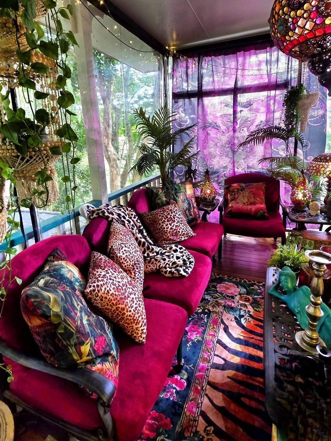 Red velvet sofa with leopard print pillows in a maximalist room with purple curtains.