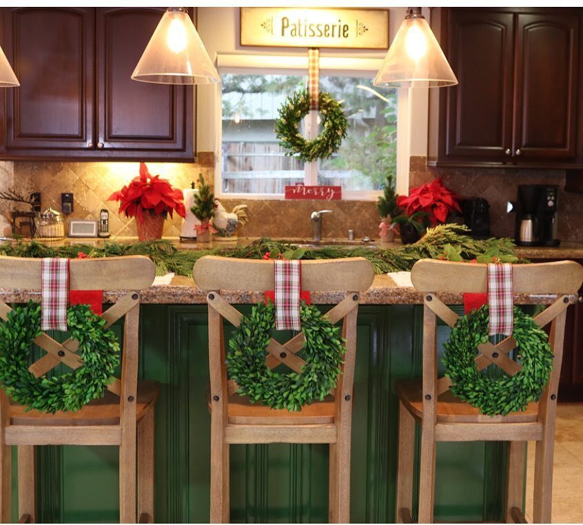 Three wooden bar stools with green wreaths and plaid ribbons lined up at a green kitchen island.