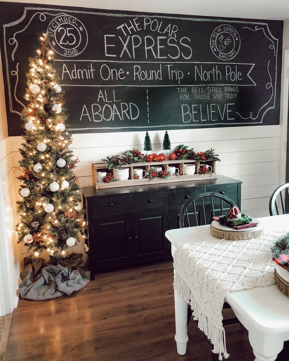 Large chalkboard with Polar Express text hanging above a decorated dark sideboard and Christmas tree.