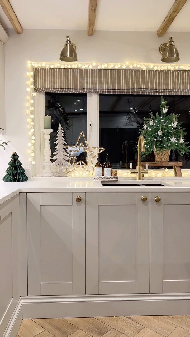 Christmas decorations including fairy lights, small trees, and candles on a kitchen window sill.