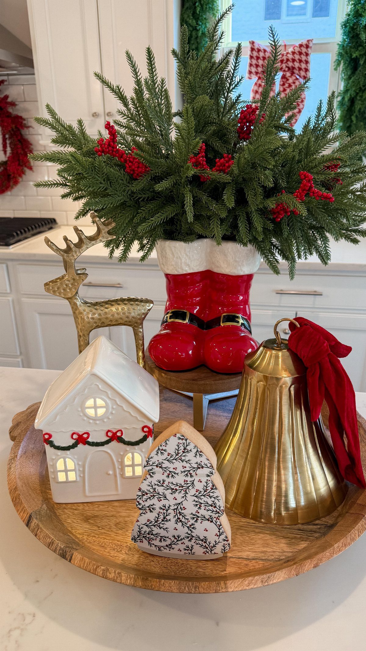 Festive Christmas decorations including a red boot vase, gold bell, and reindeer on a wooden tray.