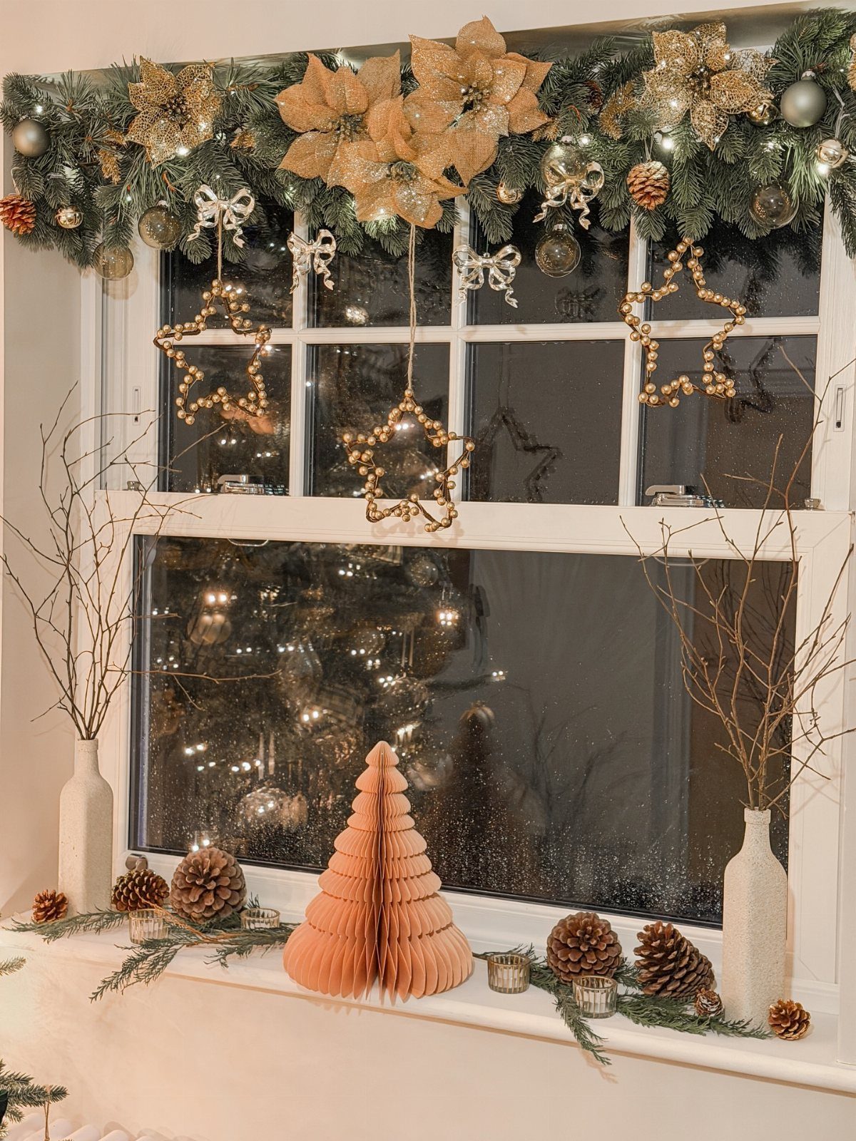 Green evergreen garland with gold poinsettias and hanging star decorations across a kitchen window.