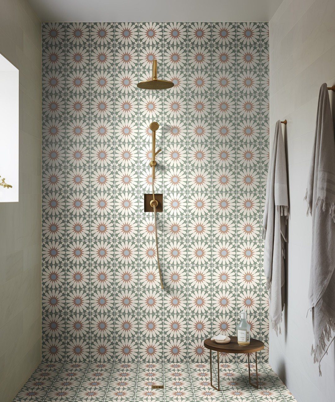 Patterned teal and terracotta starburst tiles covering a shower wall and floor with gold fixtures.
