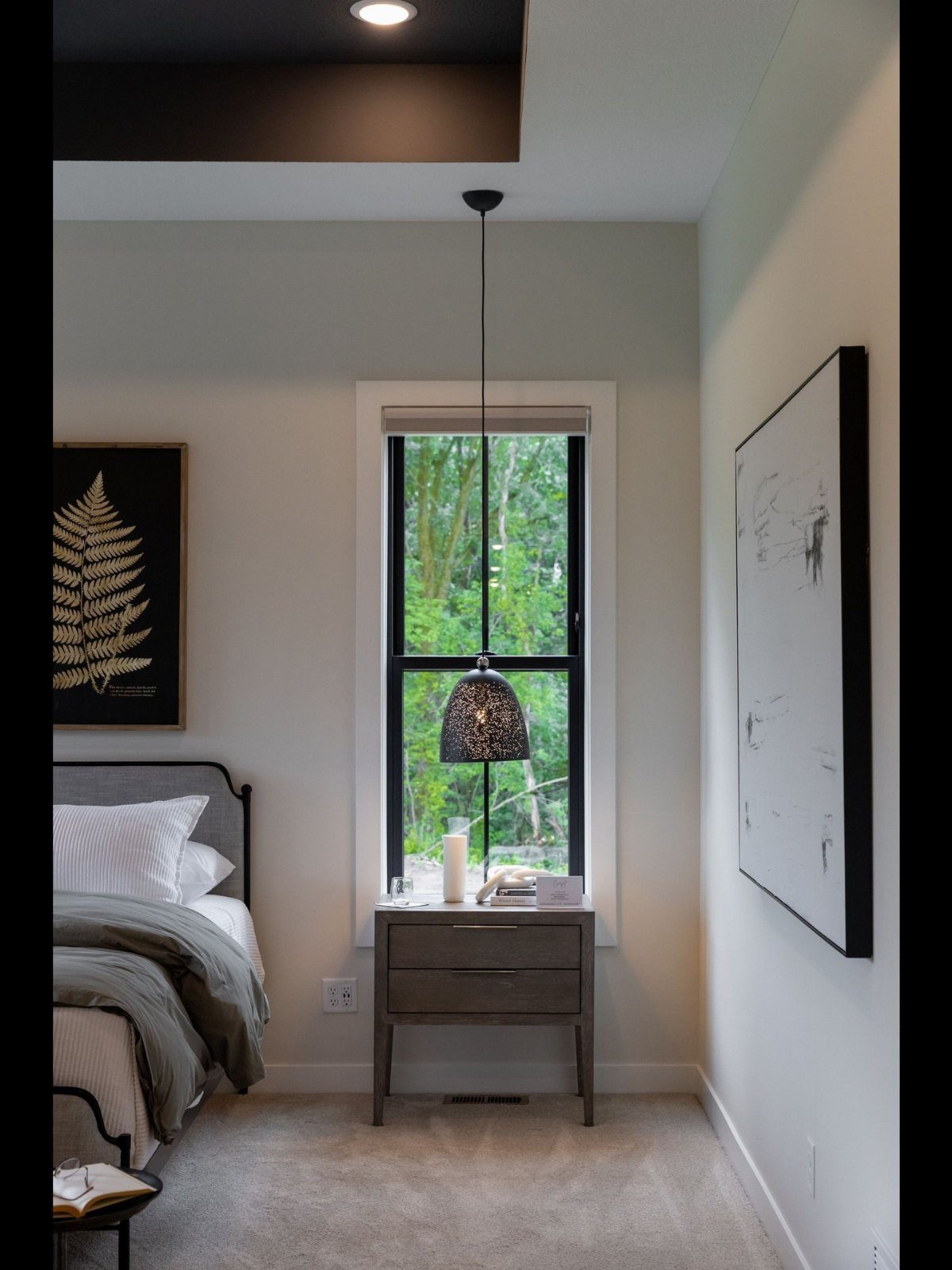 A bright bedroom with a large window overlooking green trees and a cozy bed.