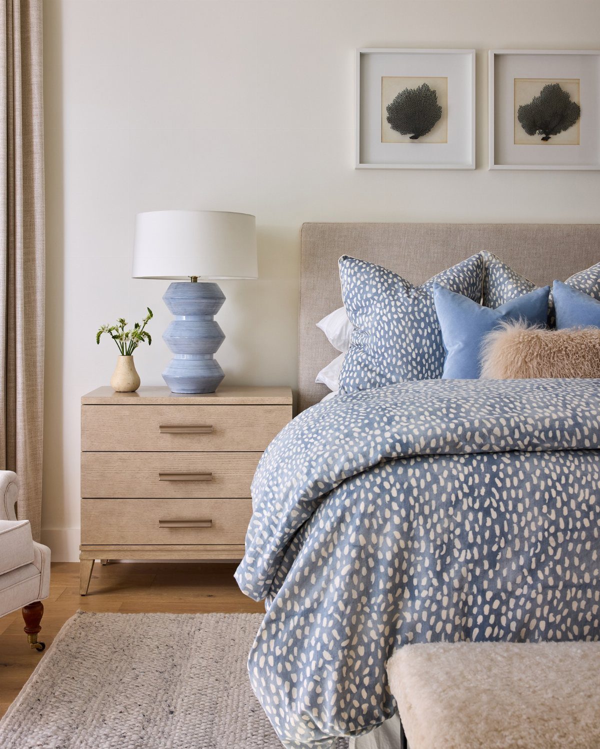 Blue patterned bedding and pillows on a bed next to a light wood nightstand.