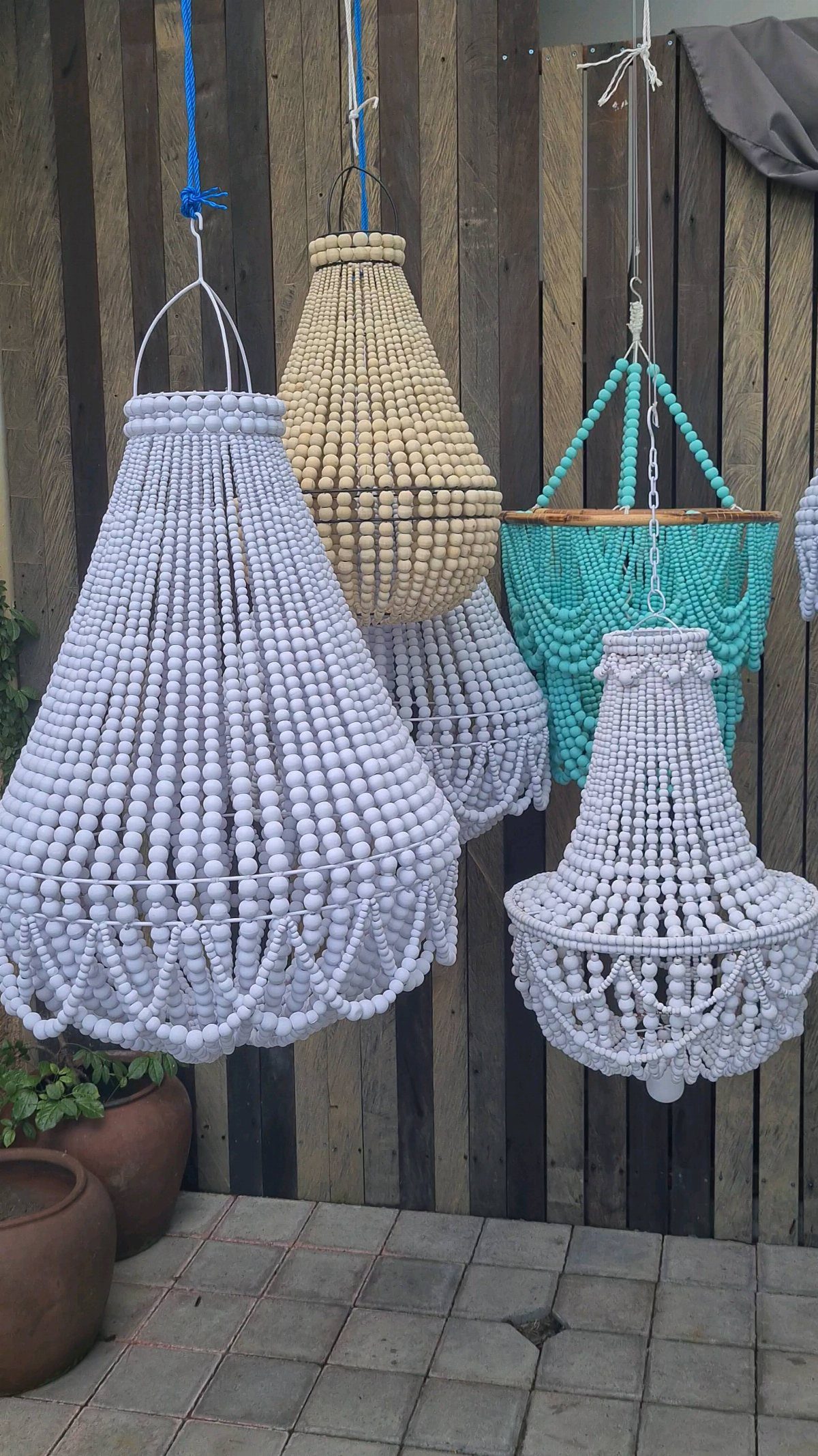 Three beaded chandeliers in white, cream, and turquoise hanging against a wooden fence.