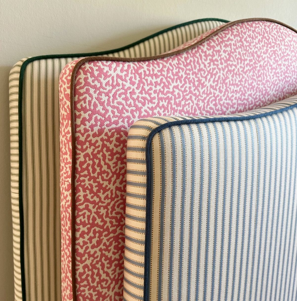 Three patterned upholstered headboards with curved tops leaning against a neutral wall.