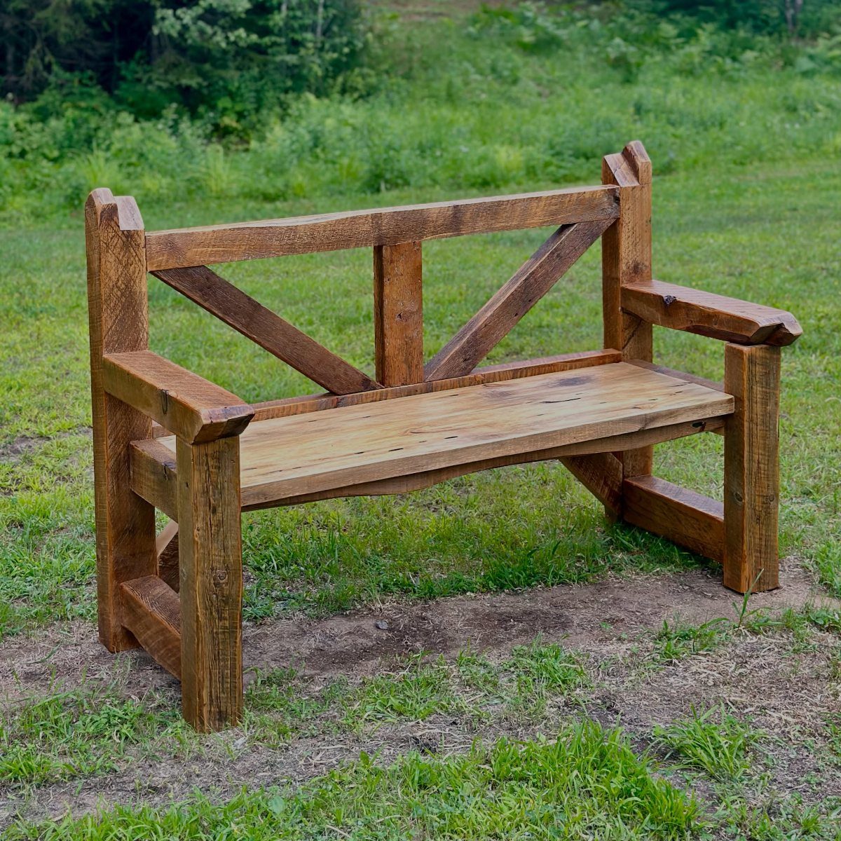 A rustic wooden bench made of weathered timber planks sitting on green grass.