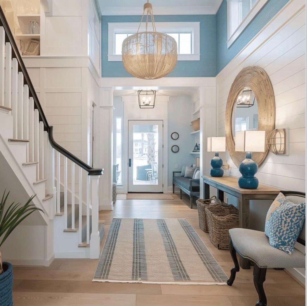 Coastal entryway with blue lamps, a woven mirror, and a striped rug on light wood floors.