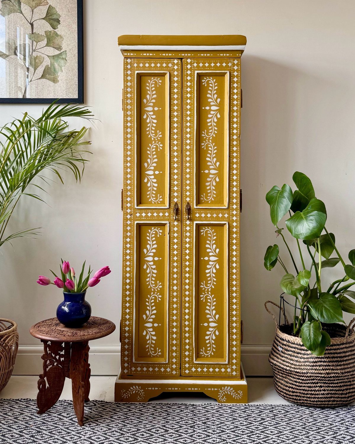 Mustard yellow patterned cabinet standing in a bright entryway with plants and flowers.