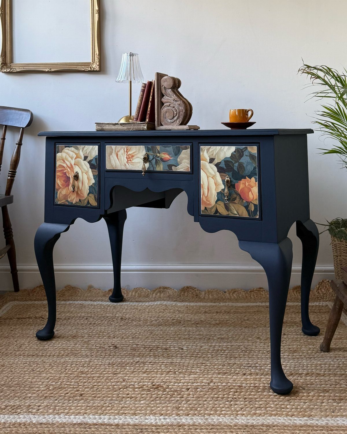 Dark blue floral console table styled with a lamp and books on a jute rug.