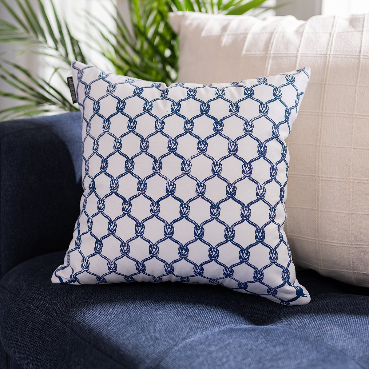 White pillow with blue rope knot pattern resting on a navy blue sofa.