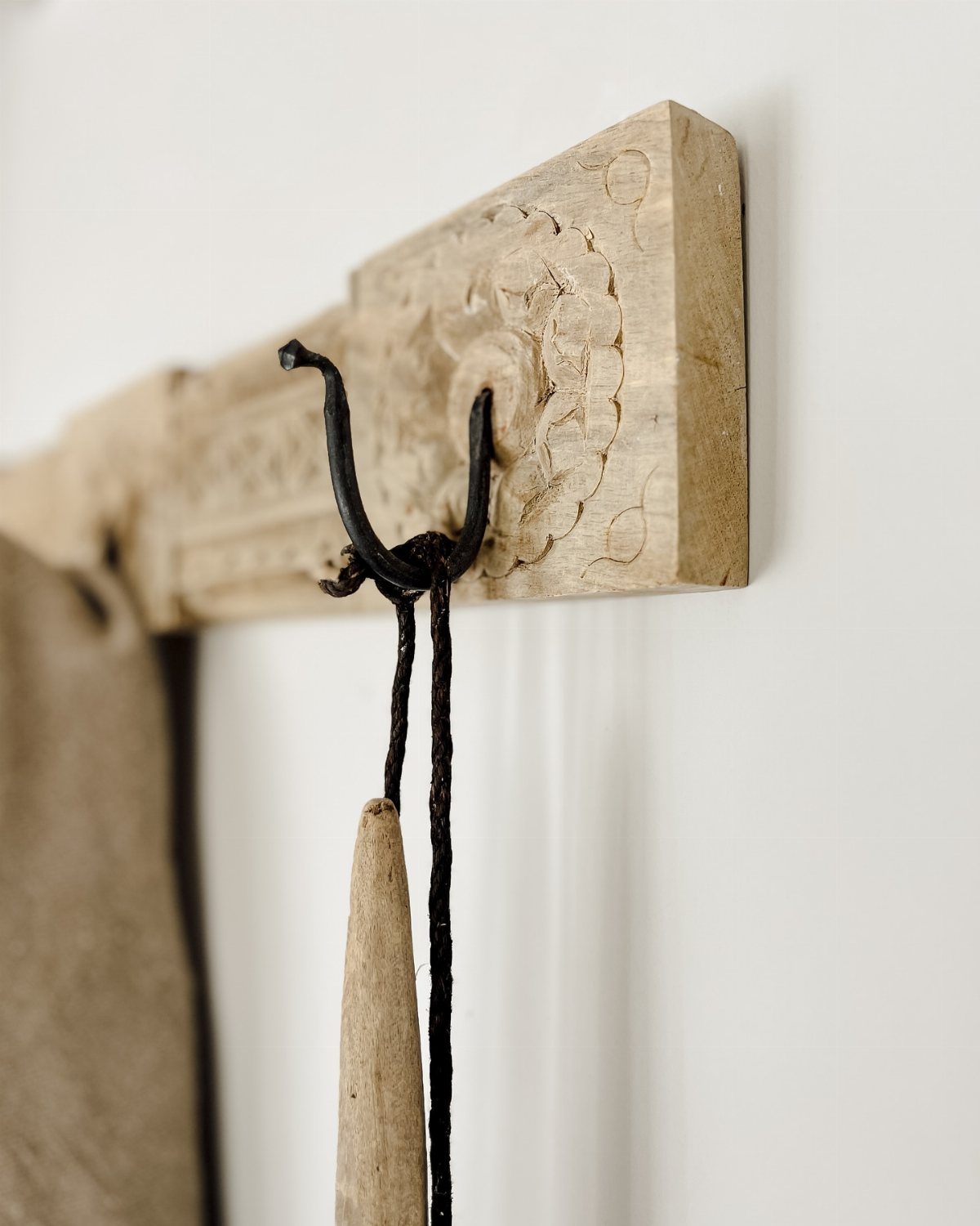 Carved light wood wall rack with a black metal hook against a white wall.