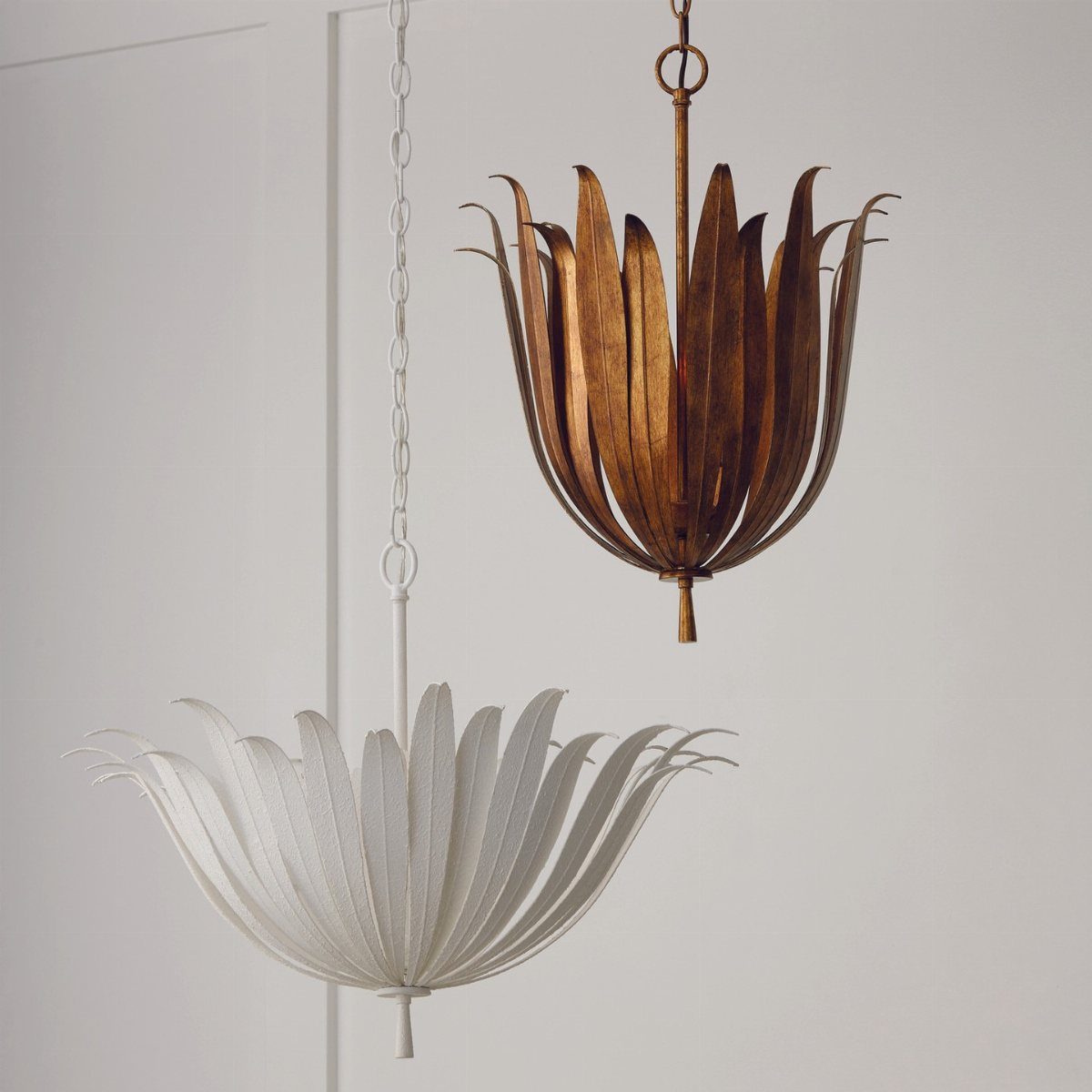 Two petal-shaped pendant chandeliers, one gold and one white, hanging against a white wall.