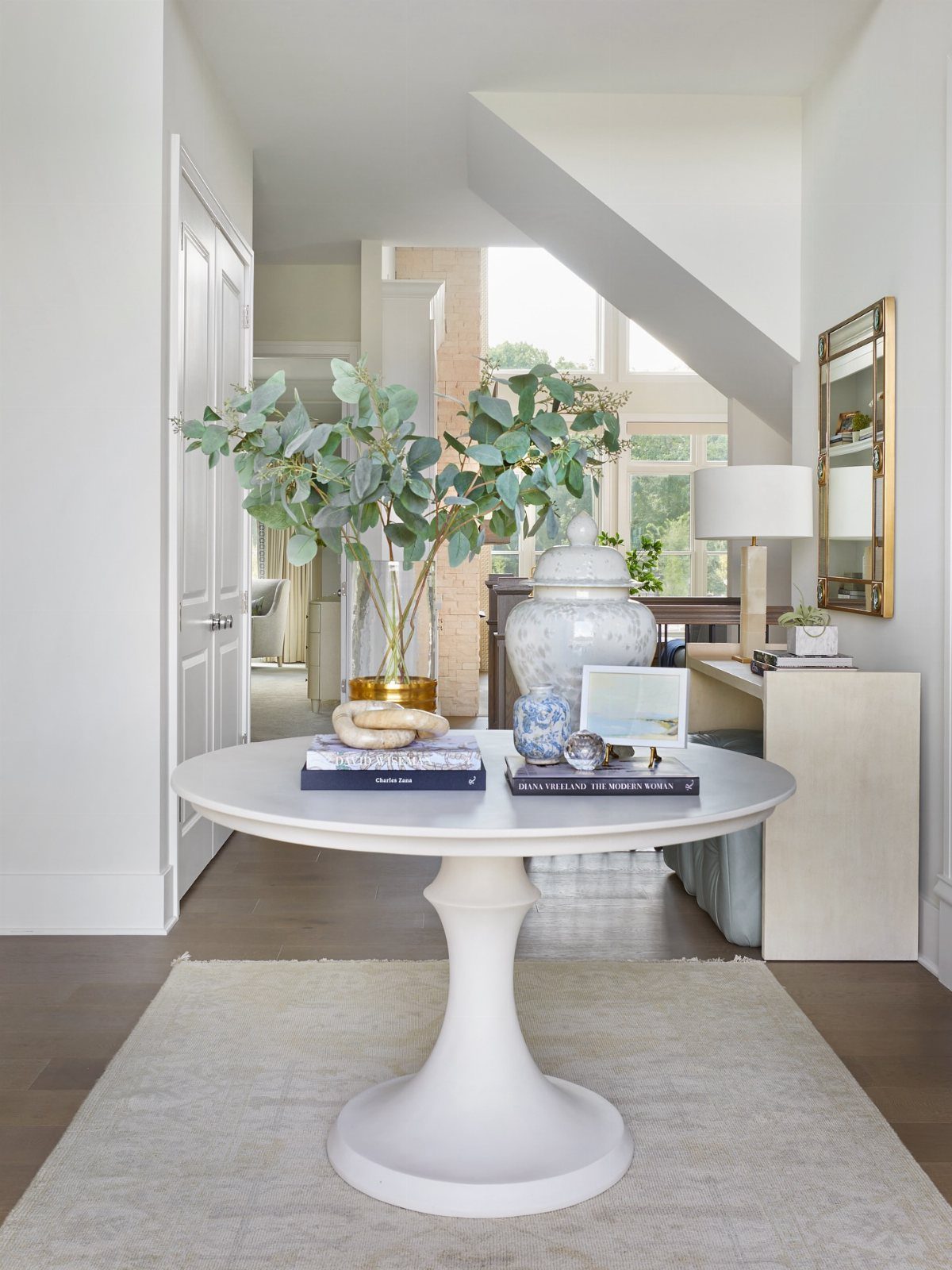 White pedestal table with greenery and decor in a bright, airy entryway.