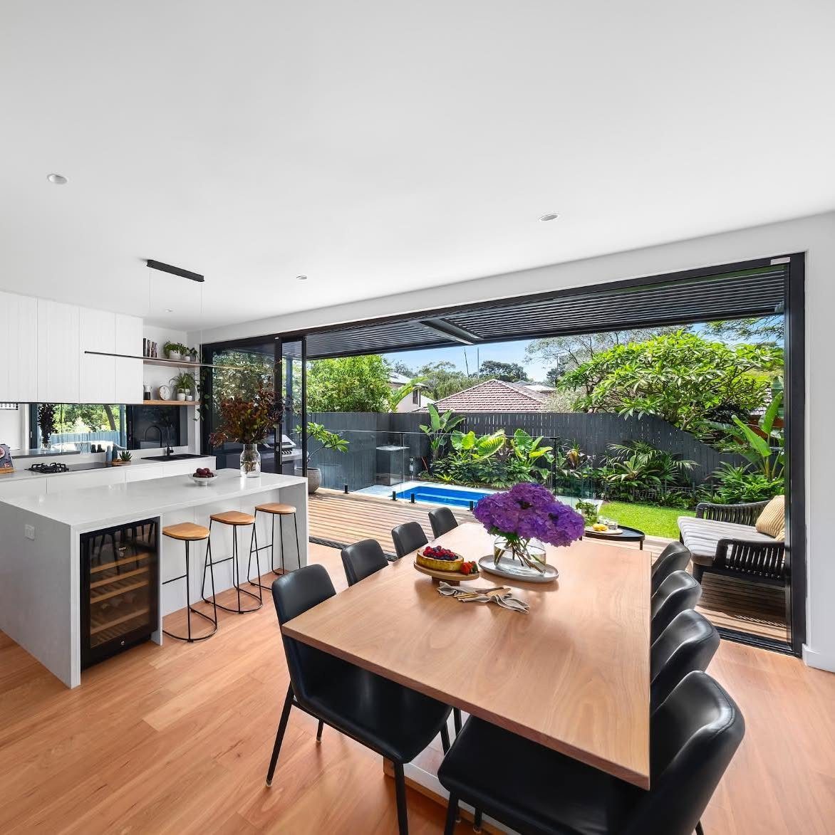 Modern dining room with large sliding glass doors opening to a backyard pool and garden.
