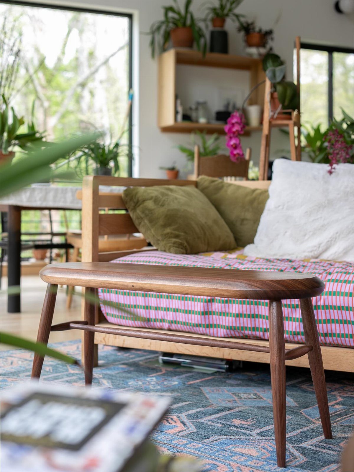 Wooden daybed with patterned cushions and green pillows on a blue patterned rug.