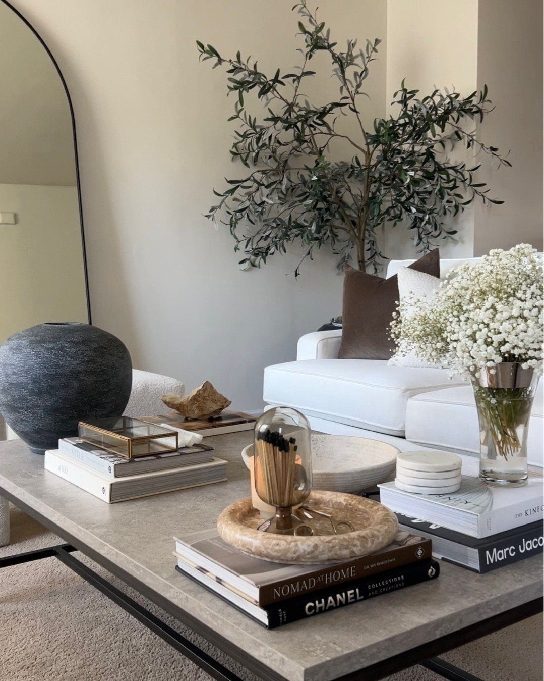 Curated decor items including books, a blue vase, and a glass cloche on a stone coffee table.