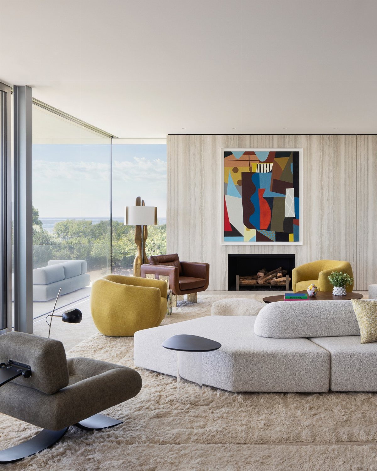 Modern living room with modular grey sofa, yellow armchair, and large abstract art overlooking the ocean.