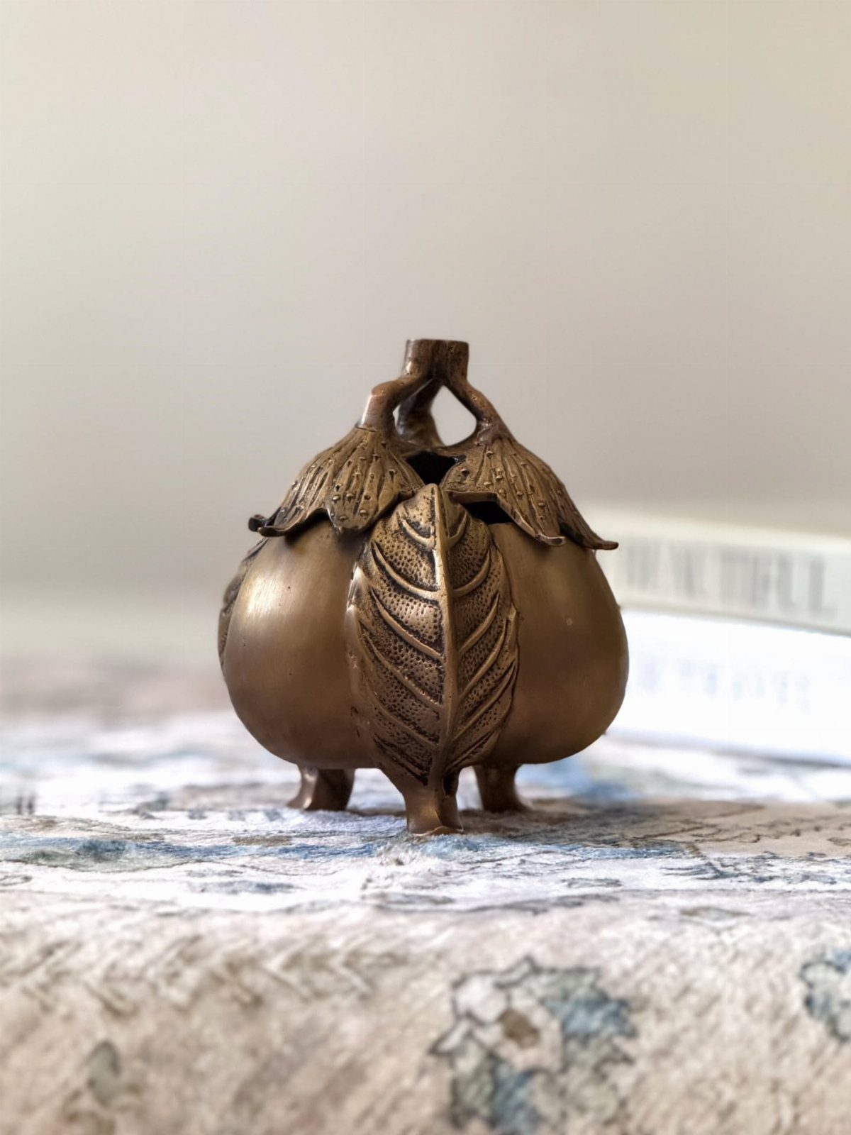 A bronze metal fruit-shaped decorative object with textured leaves on a patterned surface.