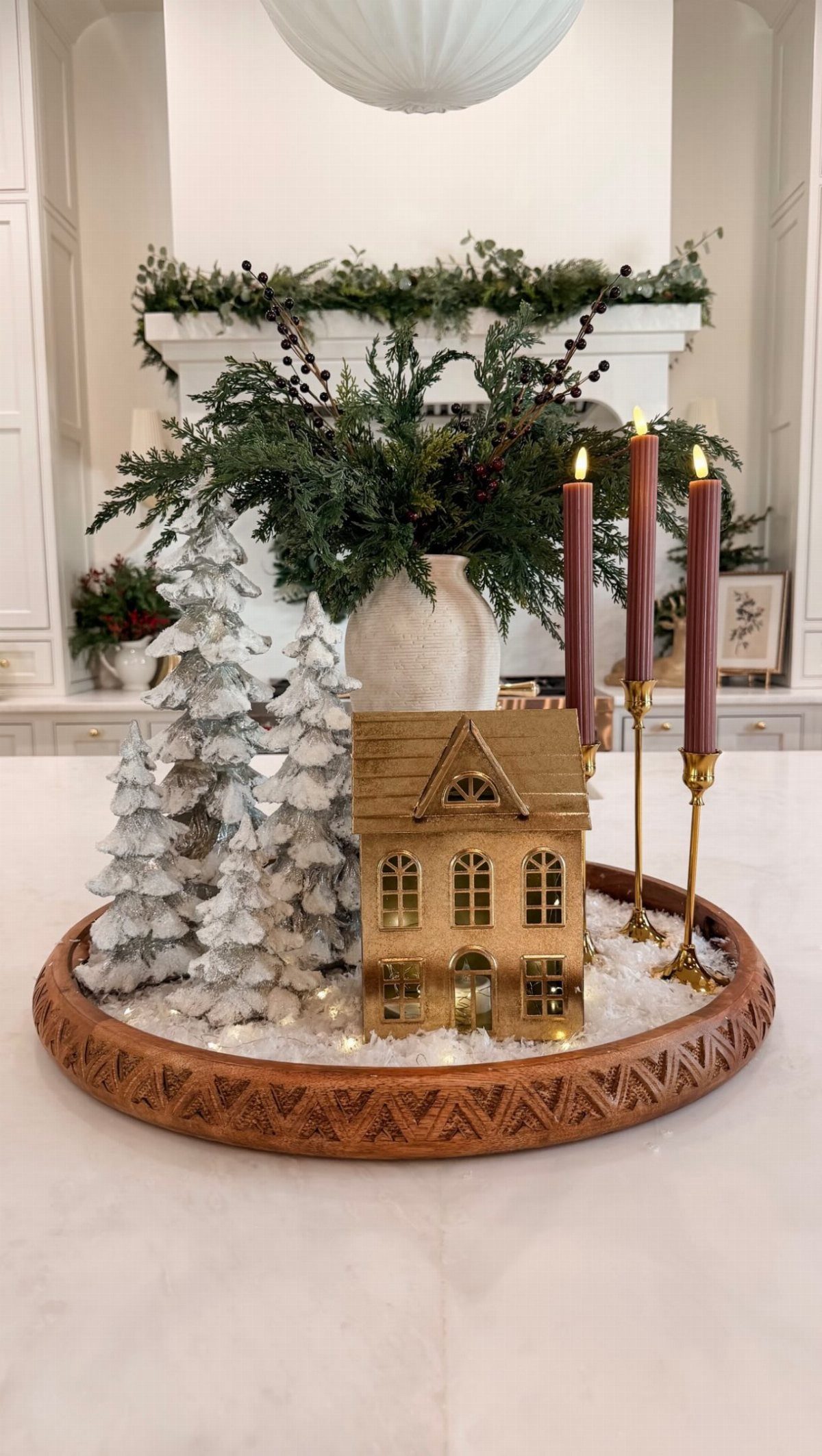 Winter seasonal decor on a wooden tray with flocked trees, a gold house, and burgundy candles.