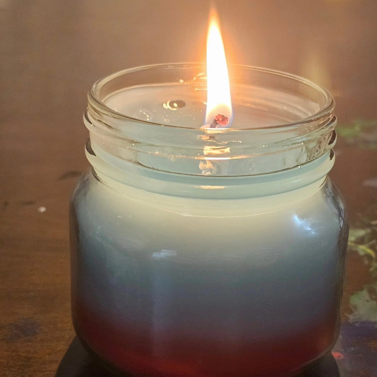 A lit candle in a frosted glass jar glowing on a dark wooden table.